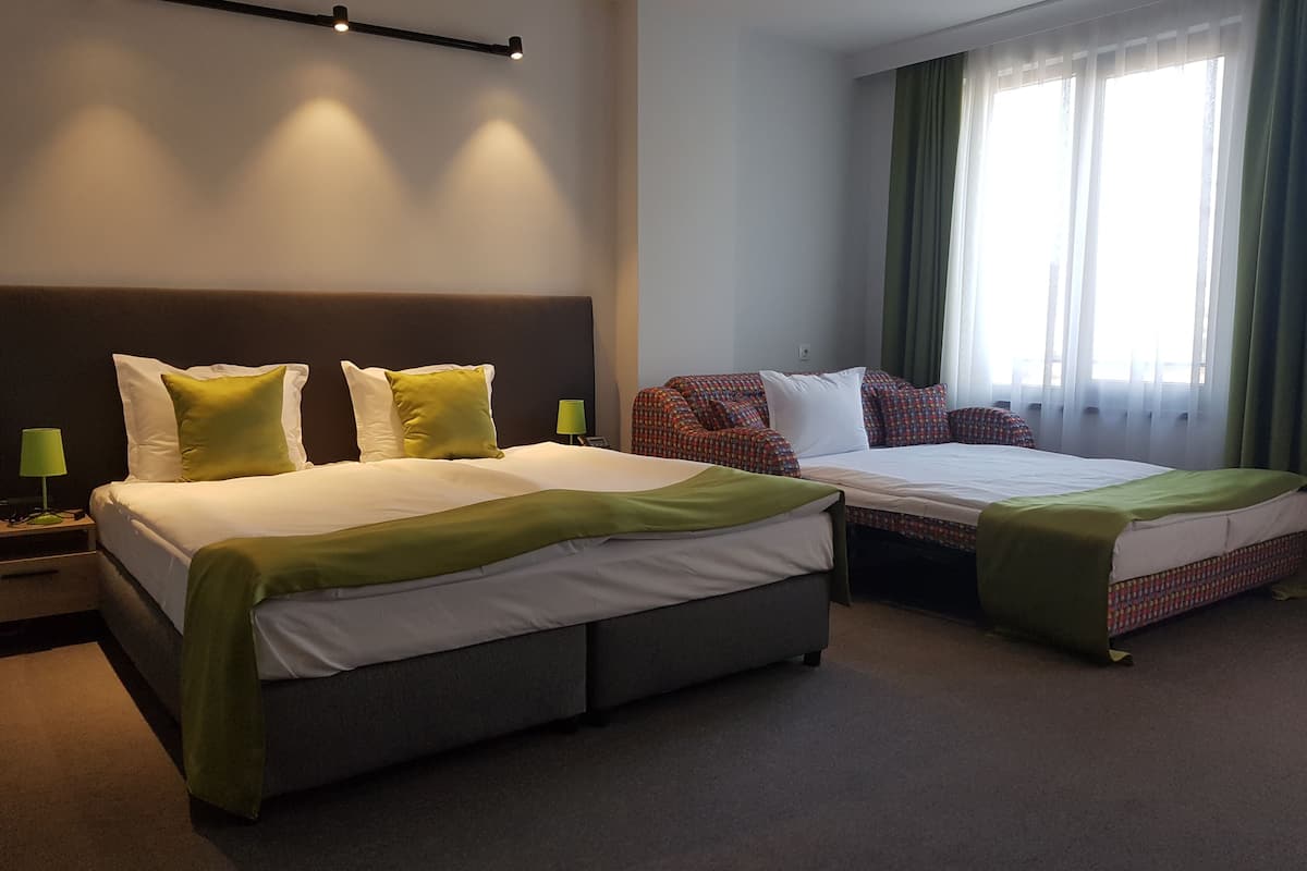 Une chambre d’hôtel avec deux lits, une tête de lit, une table de chevet avec une lampe et une fenêtre avec des rideaux.