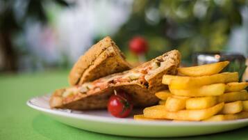 A plate with a sandwich cut in half, a stack of fries, and a cherry tomato.