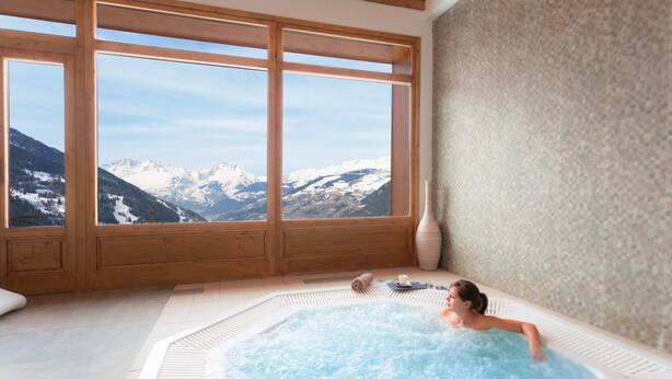 A spa room with a hot tub and a view of snow-capped mountains through large windows.