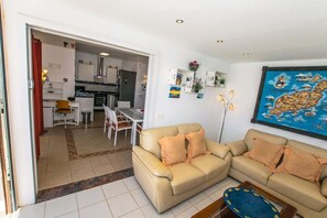 Een woonkamer met een beige bank, een salontafel en een eethoek met een witte tafel en stoelen.
