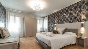 A modern bedroom with a large bed, bedside tables, a wardrobe, and a chandelier.