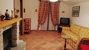 A living room with a fireplace, a sofa, a television, and a patterned curtain. - La via del bosco Apartment in a villa (Casteldelfino)