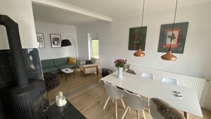 A modern living room with a sofa, a coffee table, and a dining area with a table and chairs. There is a fireplace and a radiator on the wall. - Villa Alouisia (Krusaa)