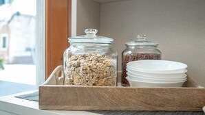 A wooden tray with a glass jar of mixed grains and a glass jar of coffee beans, accompanied by white bowls, placed on a windowsill. - Room 8 - Grifoni Boutique Hotel (Venice)