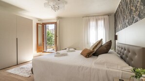 A bedroom with a large bed, a ceiling fan, a view of the outdoors through an open door, and a patterned wall. - Room 8 - Grifoni Boutique Hotel (Venice)