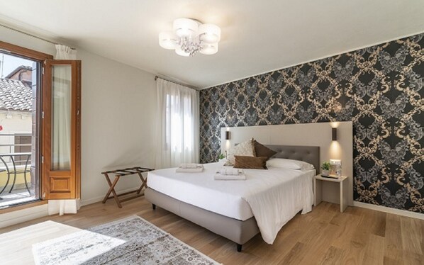 Ein Schlafzimmer mit Bett, Nachttischen, einer Chandelieber, einem Fenster mit Vorhängen und einer Wand mit Muster.