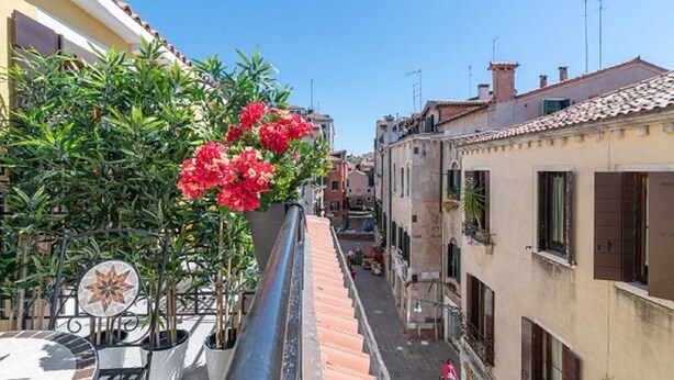 A narrow street with buildings on both sides, a tiled roof, and a potted plant with red flowers. - Room 8 - Grifoni Boutique Hotel (Venice)