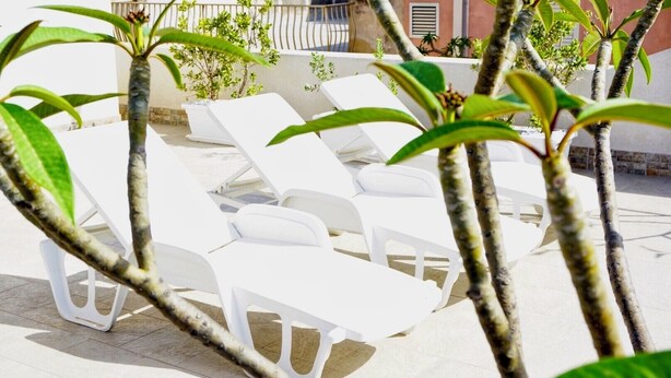 Buitenloungestoelen staan op een betegeld terras met uitzicht op een gebouw op de achtergrond.