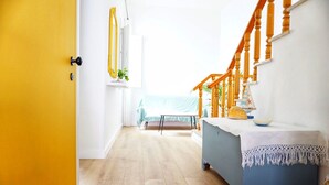 Een kamer met een houten vloer, een blauwe ladekast, een houten trap en uitzicht op de oceaan door een raam.