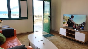 A living room with a TV, a sofa, a coffee table, and a view of the sea through a door. - Saltpeter: 1st Beach Line (Caleta de Famara)