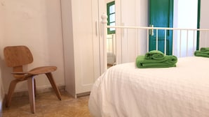 A bedroom with a bed, a chair, and a window with green shutters. - Saltpeter: 1st Beach Line (Caleta de Famara)