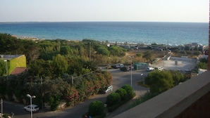 Vista costera con una carretera que lleva a una playa, rodeada de vegetación y coches estacionados.