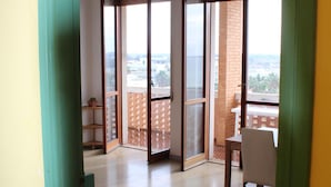 Un balcón abierto con vista a la ciudad, una mesa de comedor con sillas y una planta en maceta.