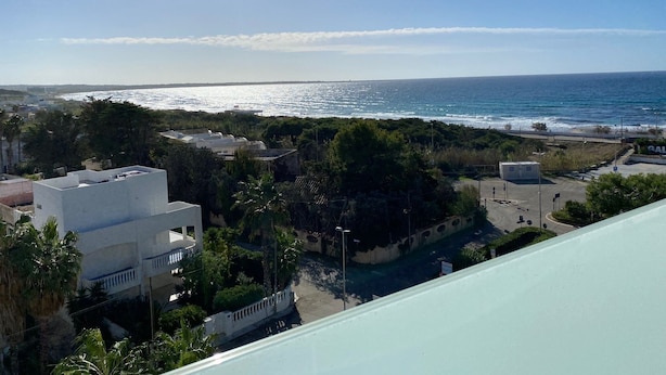 Vista costera con cielo despejado, una playa y edificios con balcones que dan al mar.