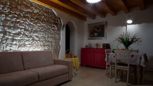 Un salon chaleureux avec un canapé beige, un buffet rouge et un coin repas avec une table mise pour deux personnes.