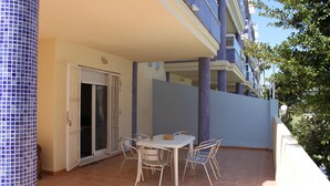 En overdækket terrasse med et bord og stole, en skydedør og en flisebeklædt væg.