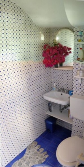 Une salle de bain avec un mur à motifs, un lavabo, un miroir, des toilettes et un tapis bleu.