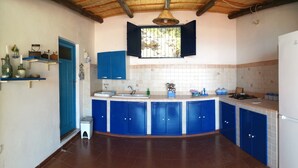 Een keuken met blauwe kastjes, witte aanrechtbladen, een witte koelkast en een raam met uitzicht op de omgeving.