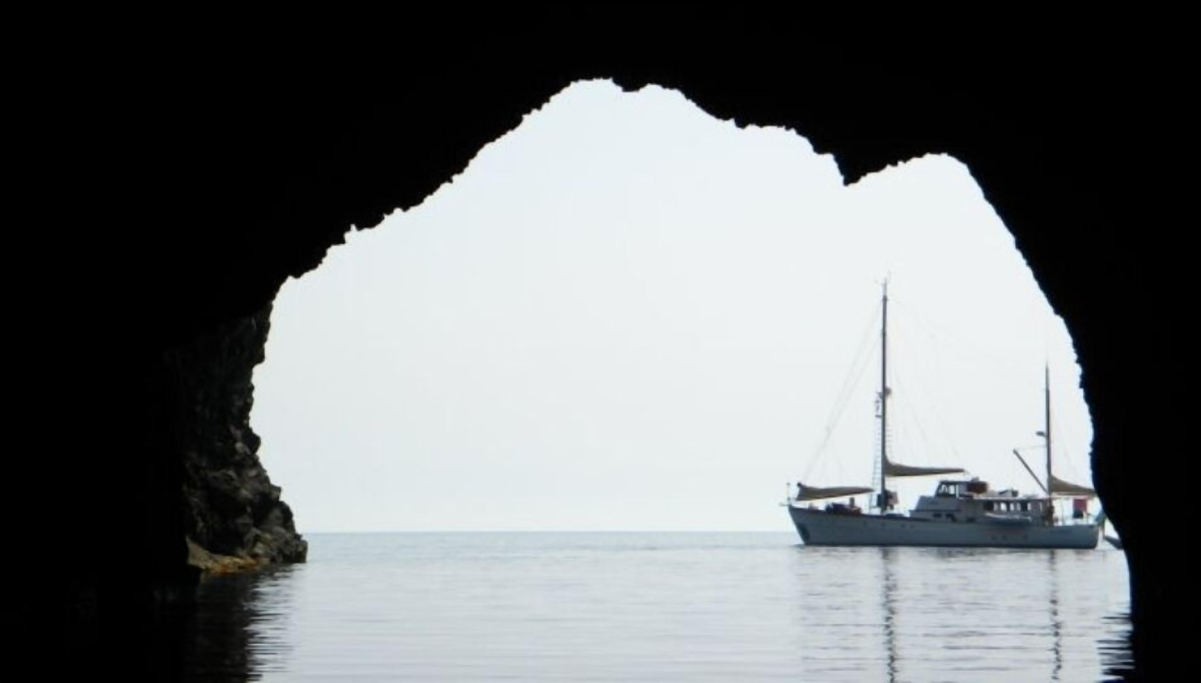 A boat in calm waters, viewed through a natural arch formation.