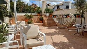 An outdoor patio with white chairs, a hanging chair, and potted plants. - Hotel La Vera Cruz (Caravaca de la Cruz)