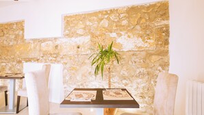 A dining area with a stone wall, a table with placemats, and two cushioned chairs. - Hotel La Vera Cruz (Caravaca de la Cruz)