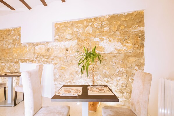 Un comedor con pared de piedra, una mesa con posavasos y dos sillas con cojines.