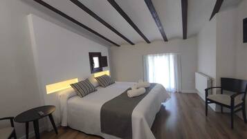 Un dormitorio moderno con una cama grande, un televisor montado en la pared, una mesita pequeña y una silla.