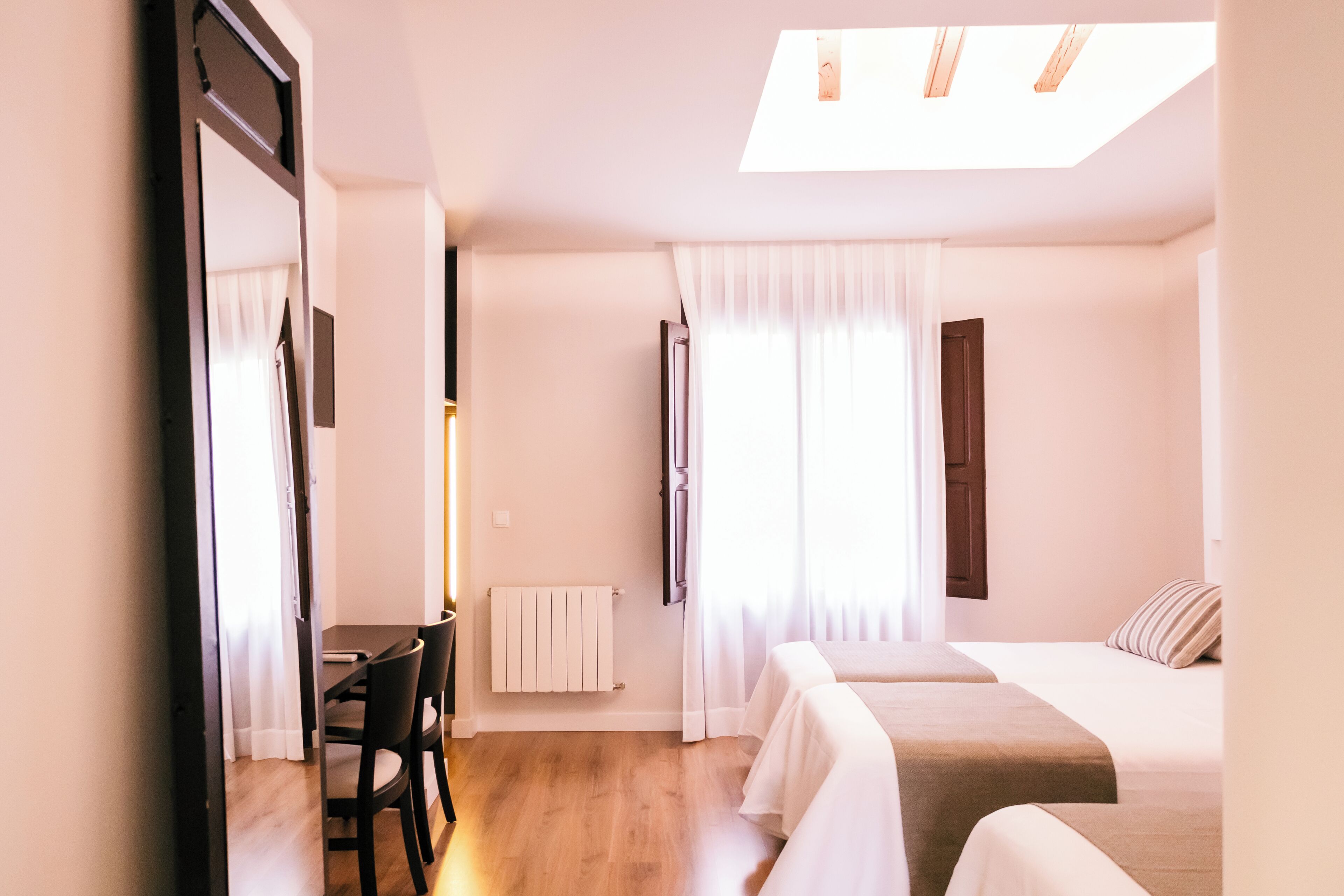 Habitació d'hotel amb un llit, una taula de nit i una cadira. Hi ha una finestra amb cortines i un òcul.