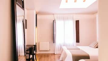 Habitació d'hotel amb un llit, una taula de nit i una cadira. Hi ha una finestra amb cortines i un òcul.