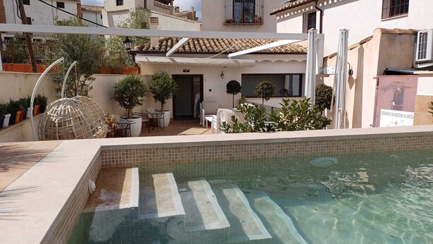 A swimming pool with a tiled edge, surrounded by outdoor furniture and potted plants. - Hotel La Vera Cruz (Caravaca de la Cruz)