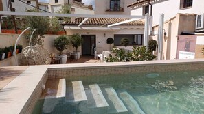 Una piscina con borde de azulejos, rodeada de mobiliario exterior y plantas en macetas.