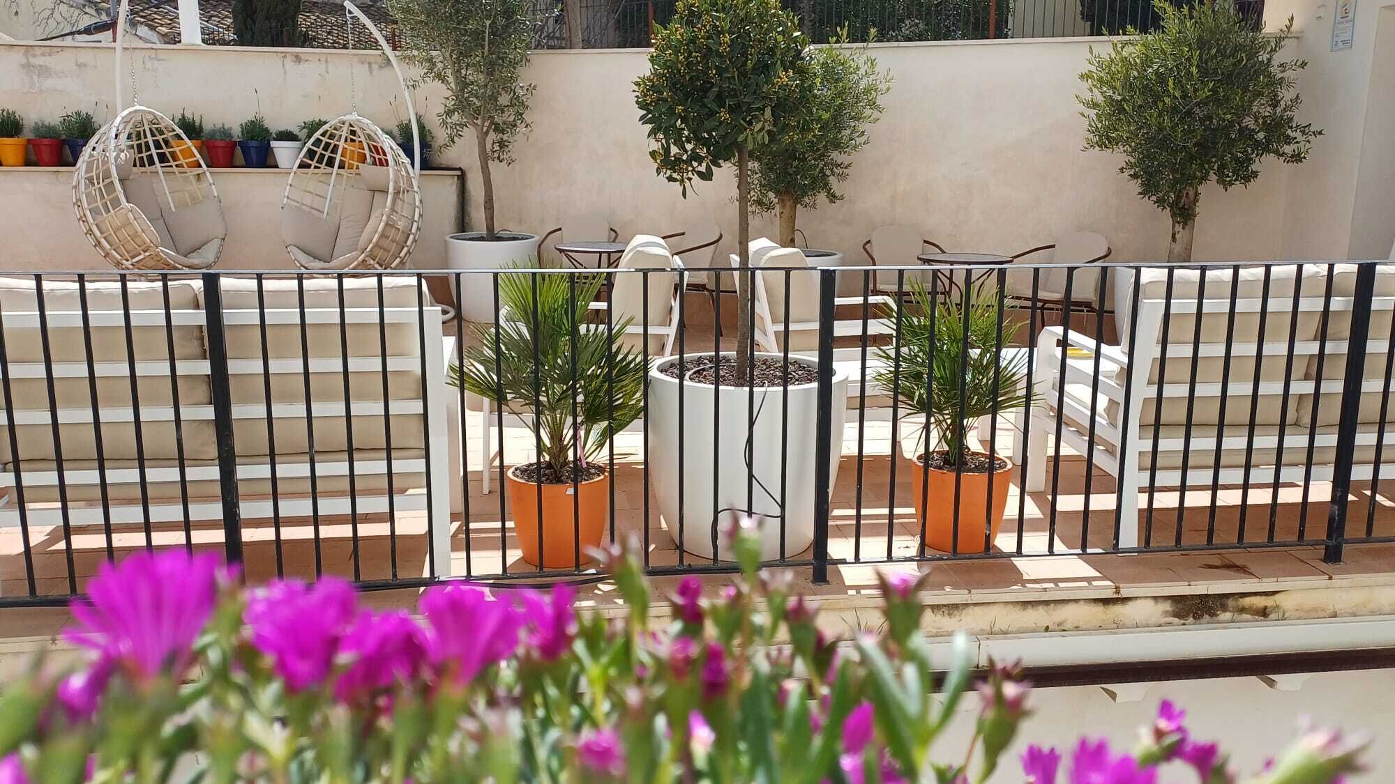 Een terras met plantenbakken, tuinmeubilair en een hangstoel.