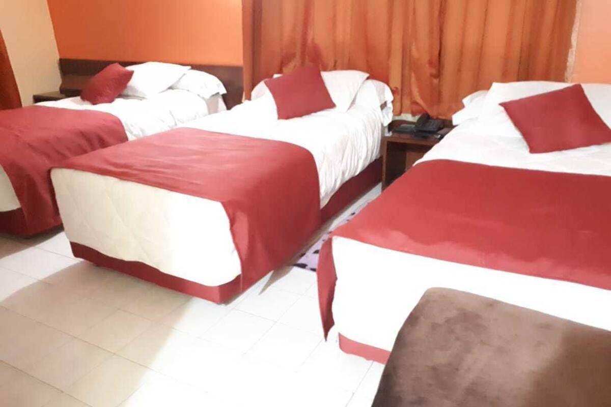 Une chambre d’hôtel avec trois lits alignés, chacun étant doté de draps blancs et de touches de couleur rouge.