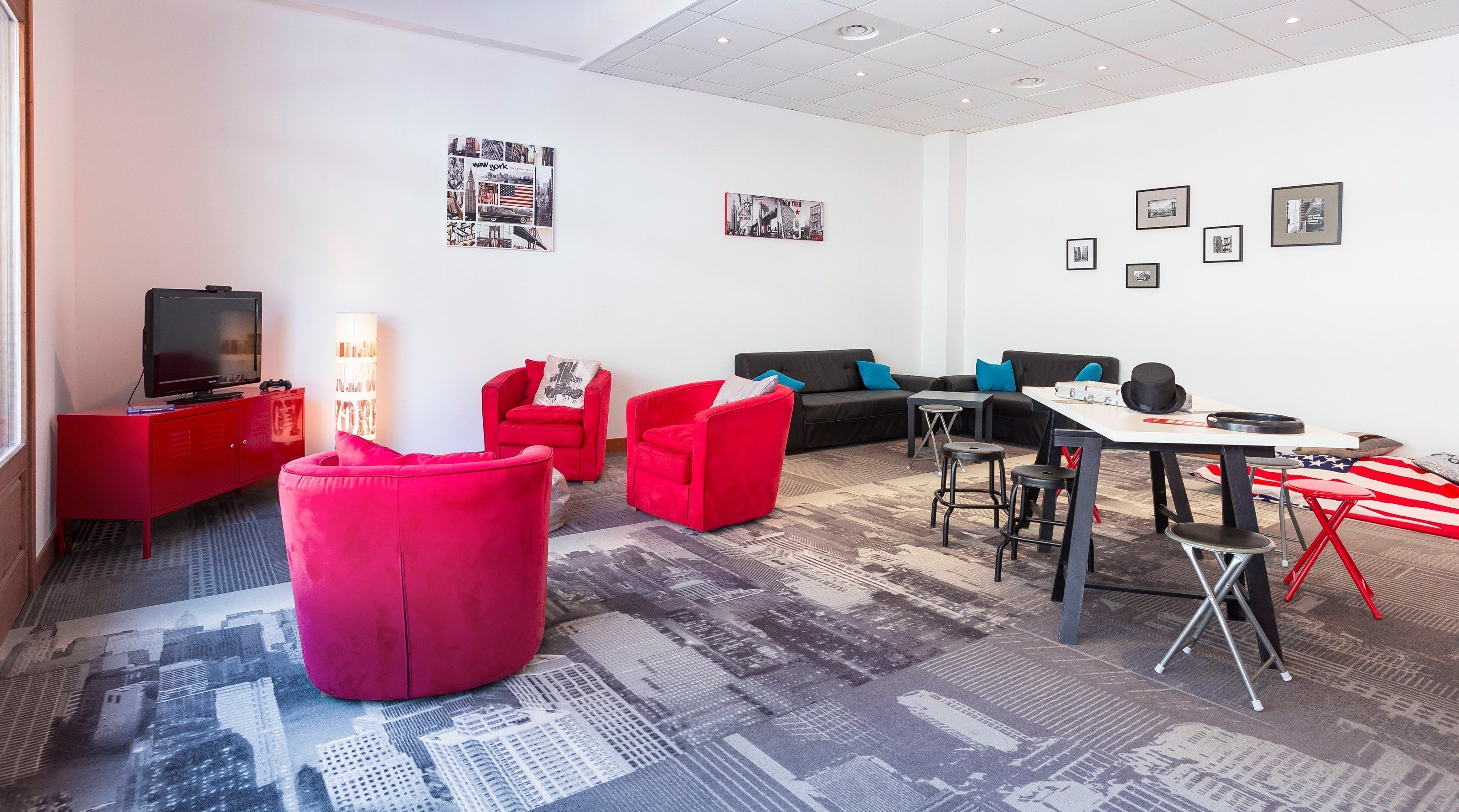 A modern living room with red furniture, a flat-screen TV, and a cityscape carpet.