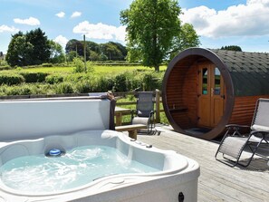 A hot tub with a wooden deck, a wooden barrel structure, and a view of a green landscape. - Rivendell Glamping Pod - UK11881 (Holsworthy, near Launceston)