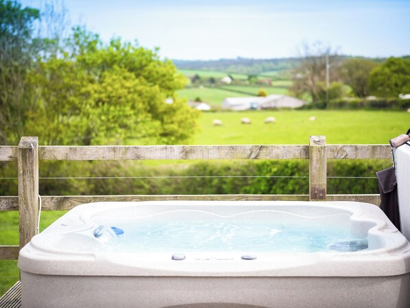 A hot tub with a view of a green field and trees.
