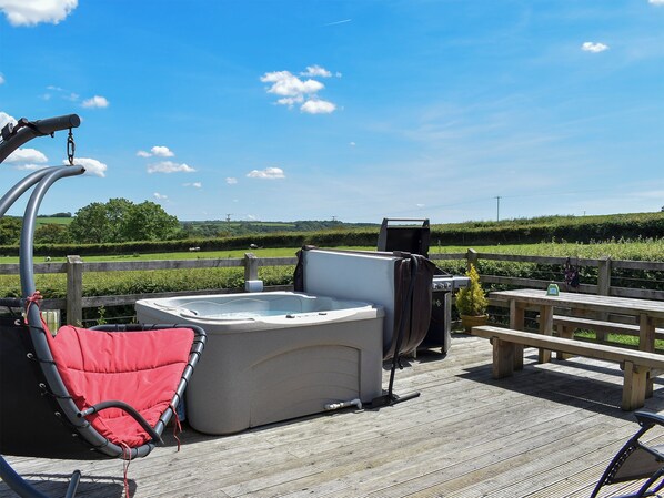 A hot tub on a wooden deck with a view of a grassy field and a wooden fence.
