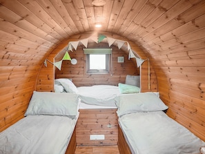 A small, cozy attic bedroom with wooden walls, a window, two beds, and a ceiling fan. - Rivendell Glamping Pod - UK11881 (Holsworthy, near Launceston)