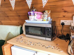 A kitchenette with a microwave, a small refrigerator, and a wooden table with a jar of snacks and a pink bag.
