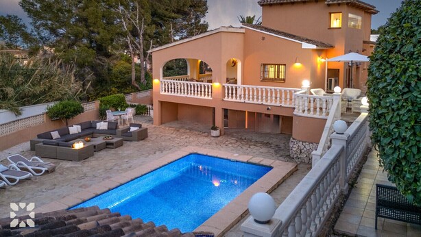 Una casa de dos pisos con piscina, mobiliario exterior y un balcón con luces.