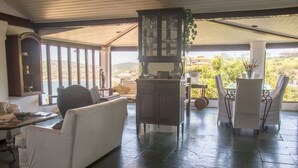 Habitación amplia con sofá blanco, aparador de madera y mesa con sillas. Amplias ventanas ofrecen vistas al exterior.