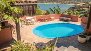 Una piscina con vista al mar, rodeada de mobiliario de terraza y plantas.