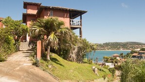 Un edificio de dos plantas con balcón, rodeado de vegetación y vistas al mar.