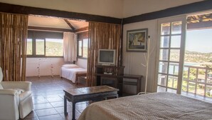 Un dormitorio con cama, una silla, una mesita, televisor y un balcón con vistas.