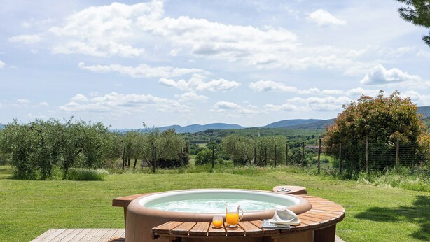 Ein Whirlpool auf einer Holzterrasse mit einer grünen Landschaft und Bergen im Hintergrund.