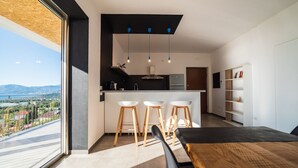Eine moderne Küche mit einer zentralen Kochinsel, Barhocker und Blick ins Freie.