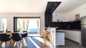 Eine moderne Küche mit Kochinsel, ein Essbereich mit Aussicht und ein Balkon mit Vorhängen.