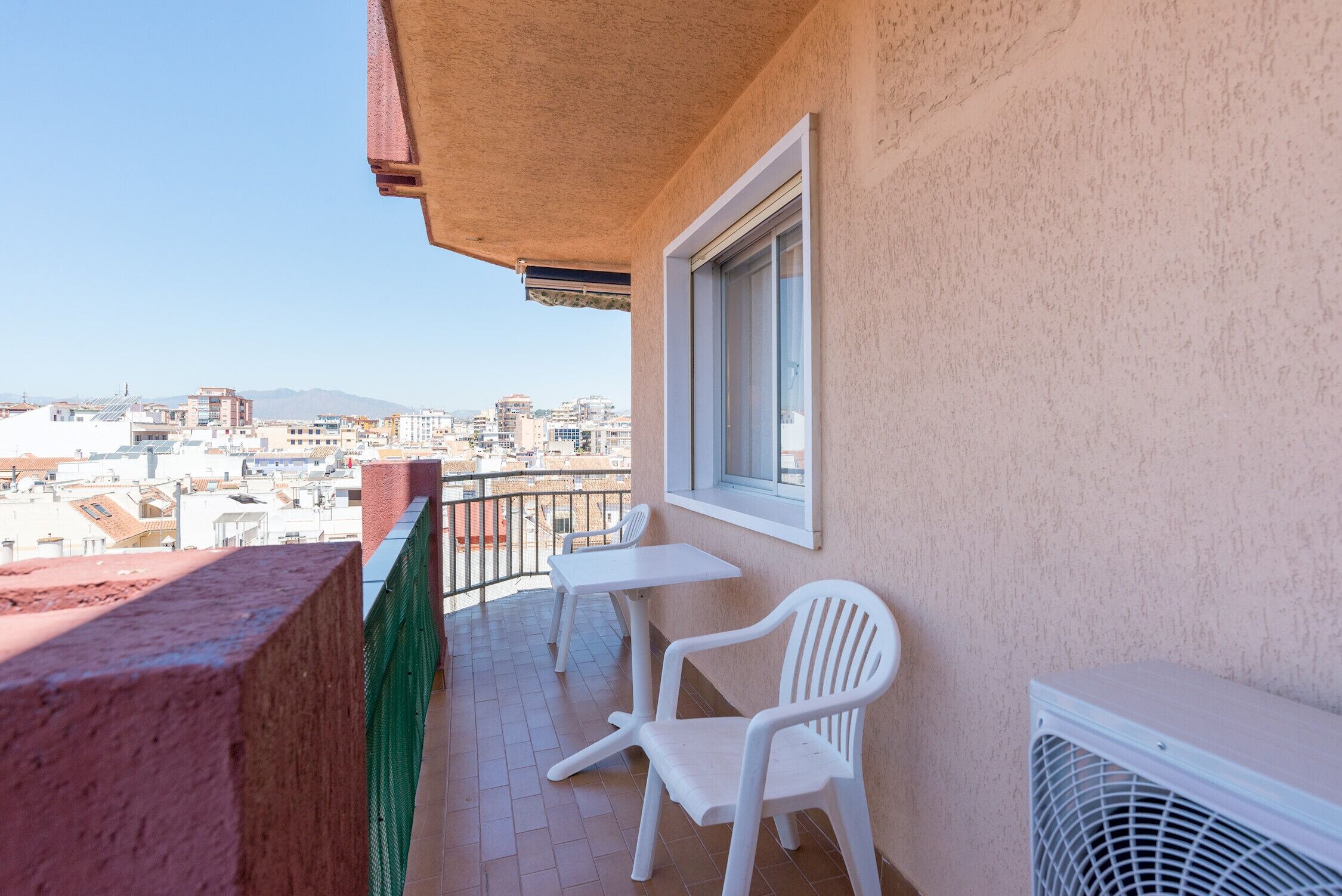Un balcón con vistas a la ciudad, una mesa blanca y una silla blanca.