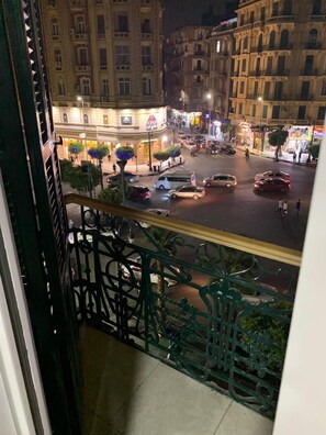 Natudsigt fra en balkon med udsigt over en travl gade fyldt med bygninger, butikker og biler.