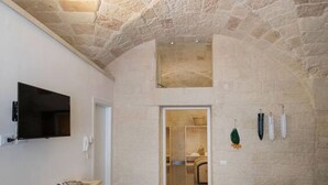 A stone-walled bathroom with a television mounted on the wall, a towel rack, and a door leading to another room. - Balbo 7 Apartment - Lecce Selection (Lecce)